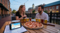 Happy couple enjoying an affordable date night with pizza and craft beer flights along Carroll Creek in Downtown Frederick, MD, with a phone displaying the Frederick subreddit recommendations.